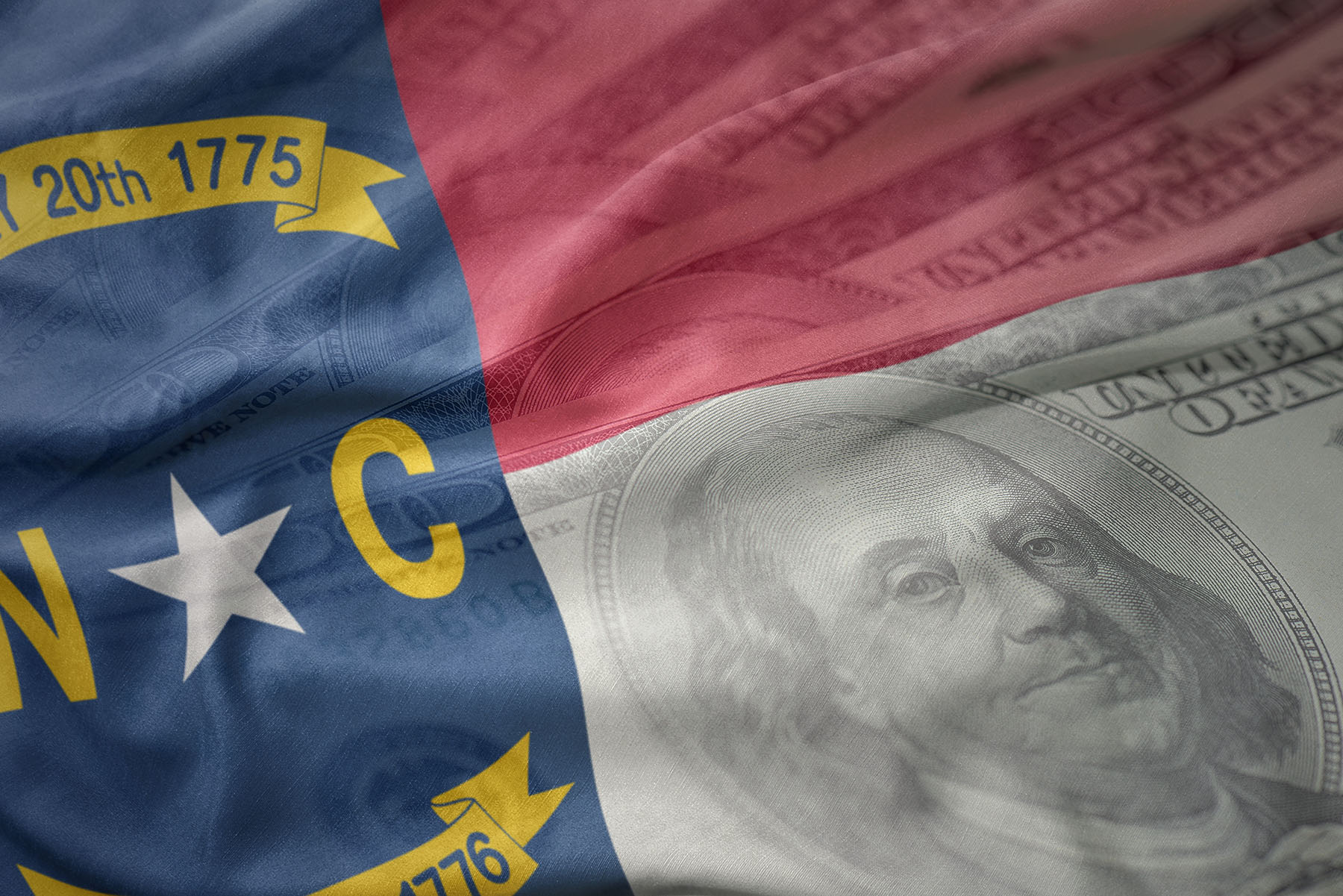 North Carolina state flag overlaid with a faint image of a U.S. hundred-dollar bill