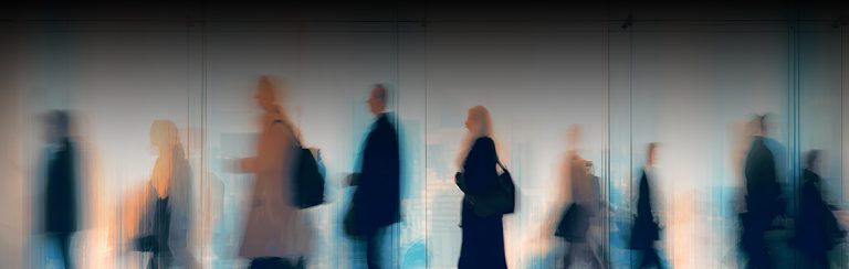 Blurry figures stride in a modern office space.
