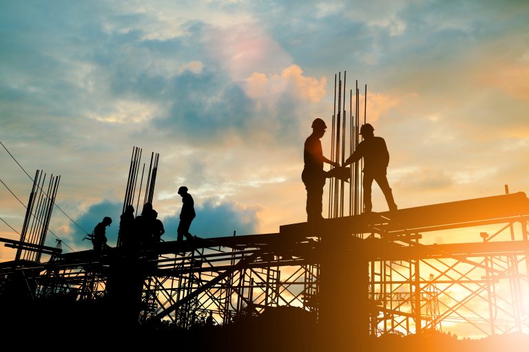 Silhouette of engineer and construction team working at site against a cloudy sunset.