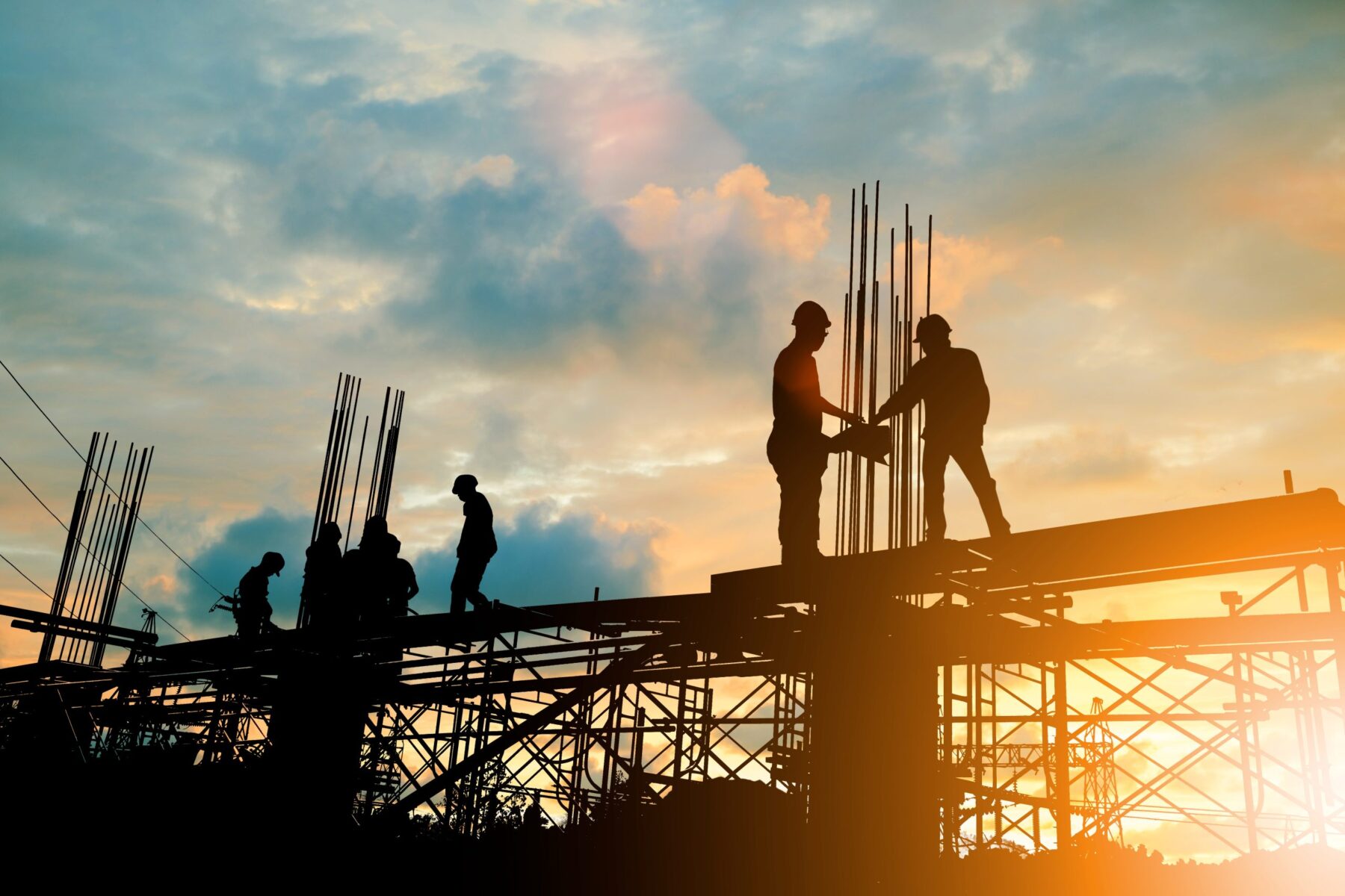 Silhouette of engineer and construction team working at site against a cloudy sunset.