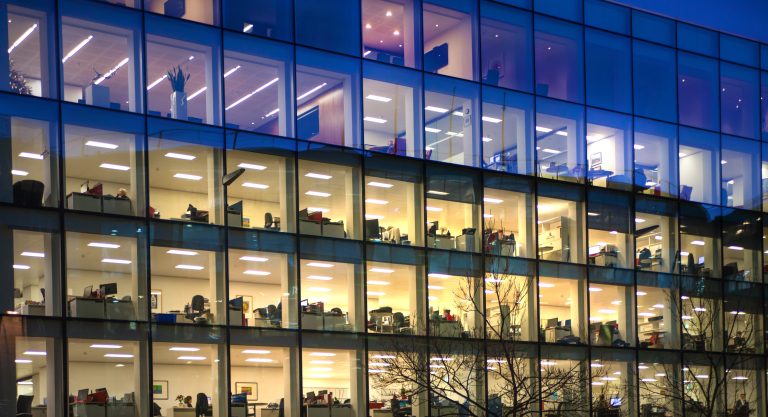 Square windows into an office building at night with silhouettes working.