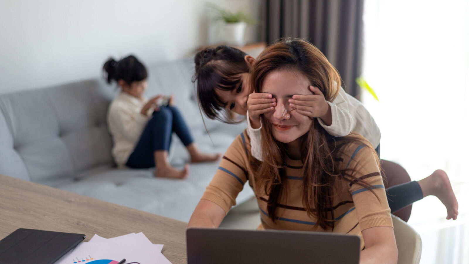 Mother working from home while child plays in background.