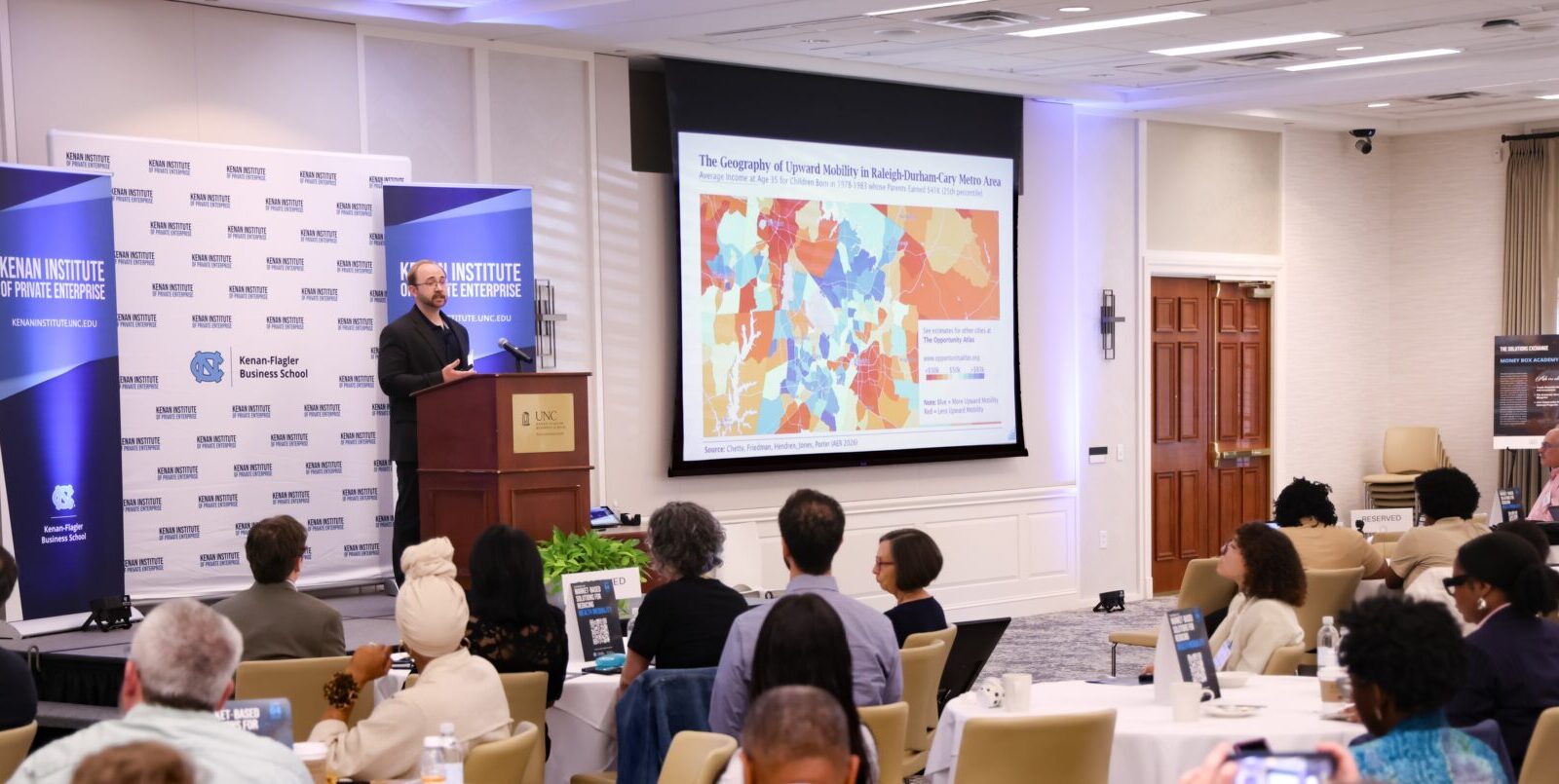 A man standing behind a podium giving a presentation to a crowd in a conference room.