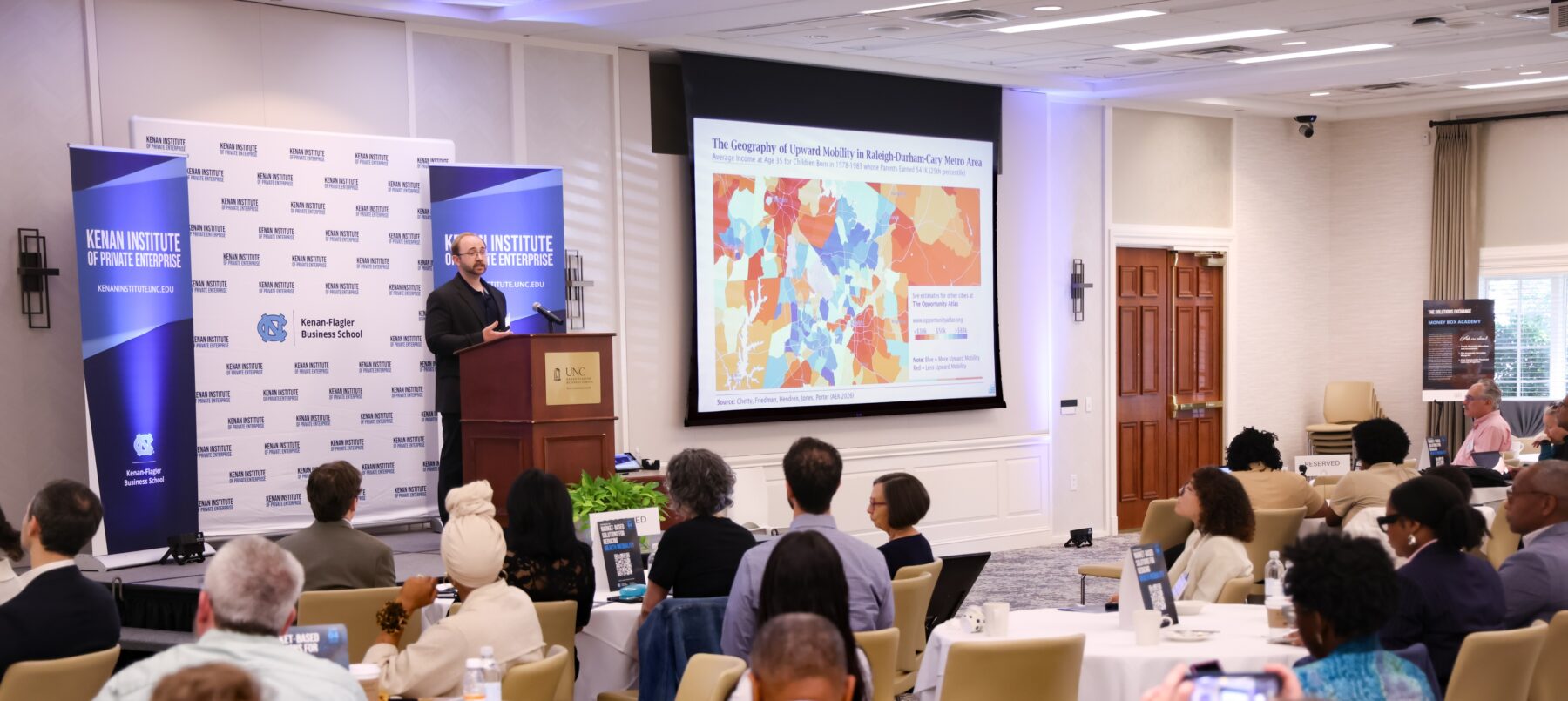 A man standing behind a podium giving a presentation to a crowd in a conference room.